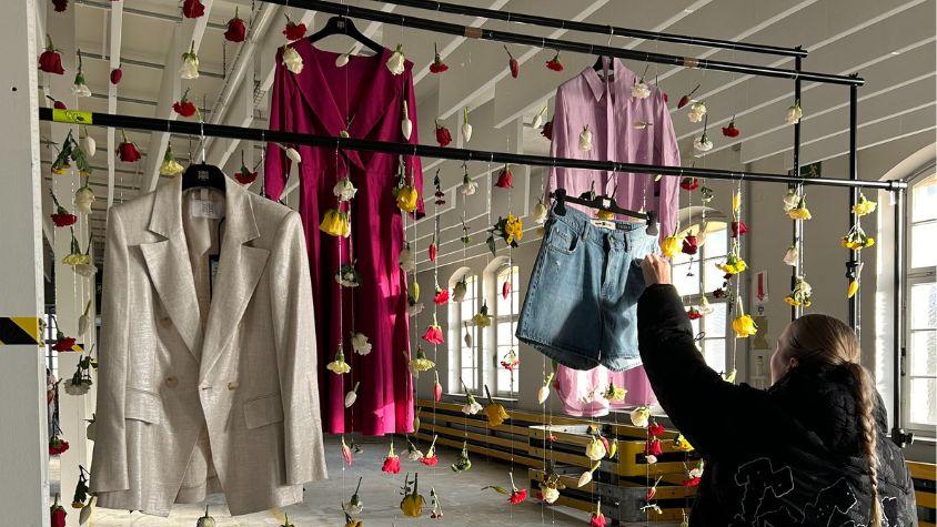 Eine junge Frau hängt Kleidung an eine Kleiderstange mit verschiedenen bunten Blumen.