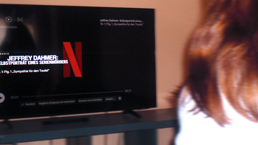 Eine Person mit langen Haaren schaut die erste Folge der Netflix-Serie " „Jeffrey Dahmer: Selbstporträt eines Mörders“ auf einem Fernseher, das Netflix-Logo ist sichtbar.