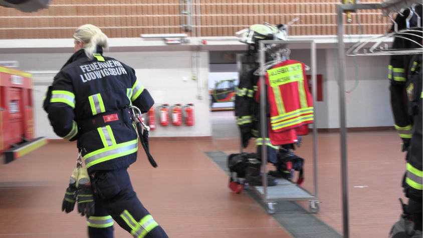 Eine Feuerwehrfrau, die ihre volle Ausrüstung an hat und schnell auf dem Weg zu einem Feuerwehrfahrzeug ist.