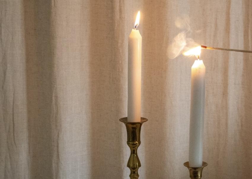 Die rechte von zwei Kerzen wird mit einem Streichholz angezündet.
