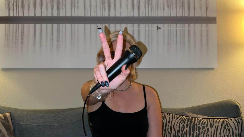 Eine junge Frau hält ein Mikrofon und zeigt das Peace-Zeichen.