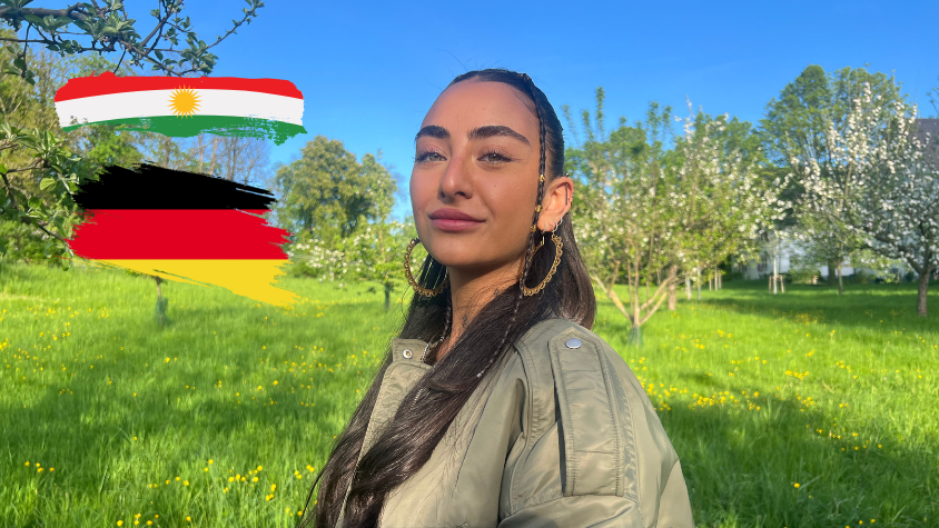 Junge Frau mit dunkelbraunen Haaren und grünen Augen, stolzer Blick in die Kamera. Nebendran sind zwei Flaggen, einmal die deutsche und kurdische.