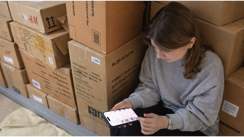 Ein Mädchen sitzt neben gestapelten Kartons und macht online Shopping.