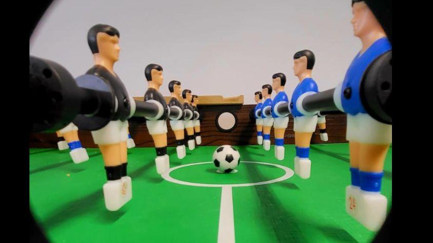 Ein Fußball liegt auf dem Anstoßkreis eines Tischkickers zwischen zwei Spielern.