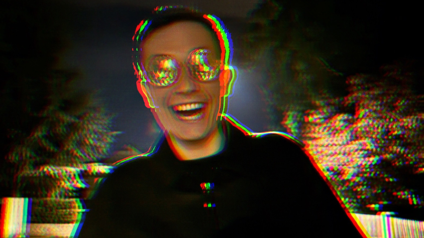 Eine männliche Person mit bunter Brille lacht verrückt in die Kamera. Die Umrisse sind etwas verzerrt