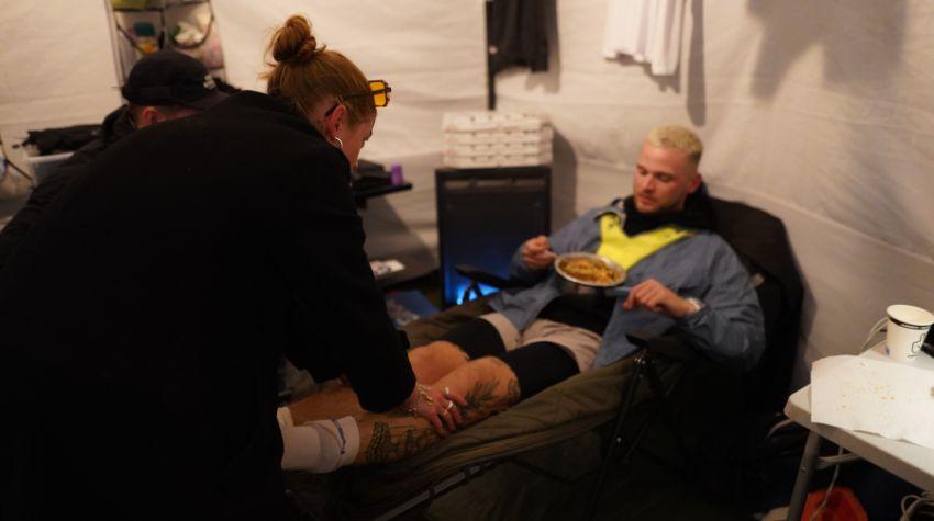 Mauritz Ehmann liegt auf einer Liege, erholt sich und isst, während eine Frau aus seiner Crew ihm die Beine massiert.
