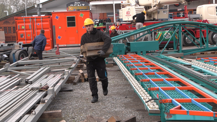 Arbeiter mit Zigarette im Mund schleppt Bauteile der wilden Maus rum