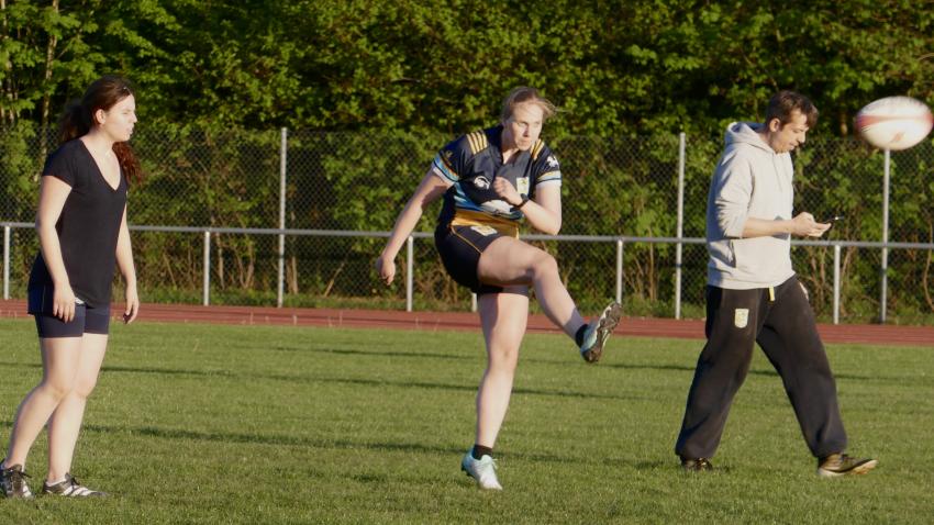 Rugby-Spielerin kickt einen Ball in die Luft.