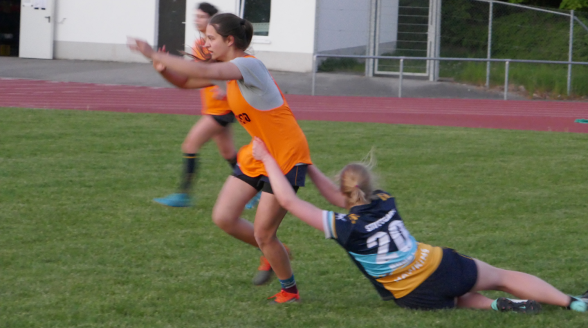 Rugby-Spielerin wird von anderer Spielerin zum Boden gezogen.