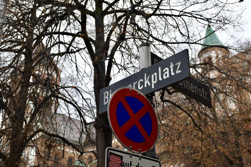 Zu sehen ist ein Straßenschild mit der Aufschrift Bismarckplatz, im Hintergrund die St. Elisabeth Kirche.