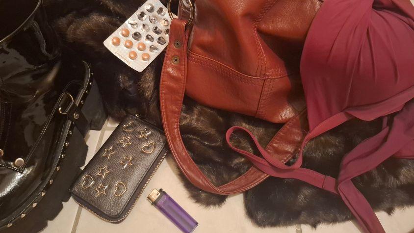 Auf einem Flurboden liegen eine rote Tasche, Tabletten, ein Fellmantel, schwarze Plateauschuhe, ein Geldbeutel und ein Feuerzeug.