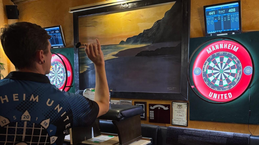 Ein Mann wirft auf eine beleuchtete Dartsscheibe 
