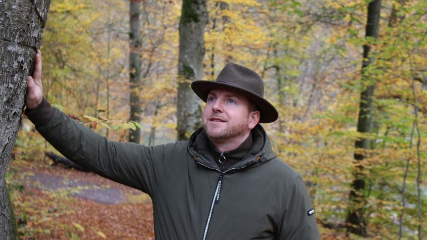 Förster Ulrich Potell lehnt sich an einen Baum und schaut in die Ferne