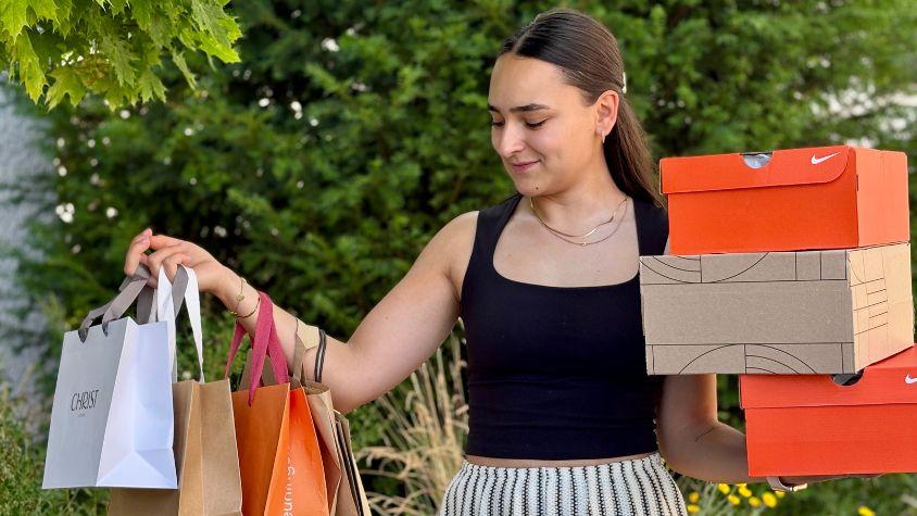 Junge Frau mit Einkaufstaschen und Schuhkartons nach einem Shoppingtrip. Das Bild symbolisiert Konsum und Retail Therapy.