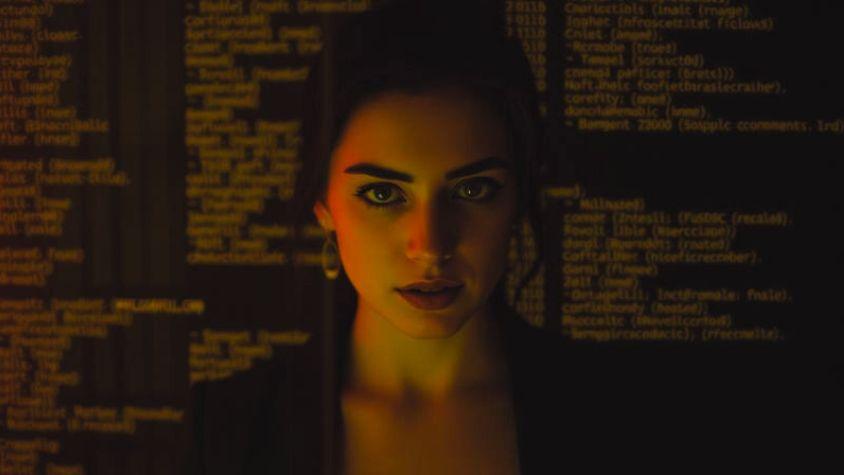 Frau, die zentral im Bild steht und geradeaus schaut. Im Hintergrund ist Code zu sehen.