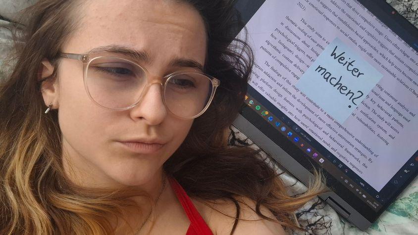 Eine Frau liegt mit erschöpftem Blick neben ihrem Laptop. Auf dem Laptop klebt ein Post-it mit der Aufschrift „Weiter machen?“.