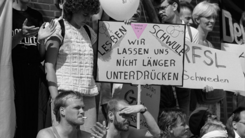 Auf dem Plakat der Demonstrierenden steht neben einem rosa Winkel "Lesben Schwule wir lassen uns nicht mehr unterdrücken".