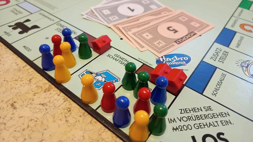 Zu sehen ist ein Ausschnitt eines Monopoly Spielbretts. Man sieht zahlreiche Spielfiguren, die um wenig verfügbaren Wohnraum konkurrieren. 