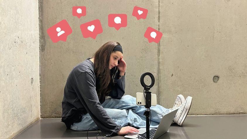 Content Creator sitzt verzweifelt auf dem Boden, Ringlicht inklusive Smartphone und Laptop liegen neben der Person. Emojis in Form von Likes, Kommentaren und Follows schweben über dem Kopf. 