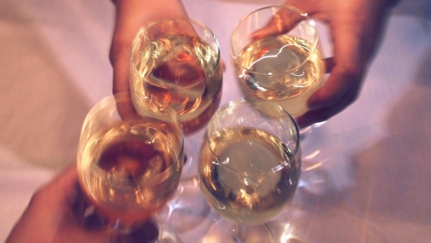 Hände die Gläser mit Weißwein halten und anstoßen.
