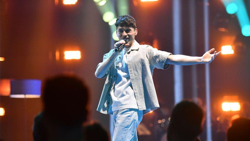 Vincent Varus beim ESC-Vorentscheid: Er ist in der Mitte des Bildes auf der Bühne, schaut beim singen frontal in Richtung Kamera. Im Vordergrund ist das Publikum zu sehen.