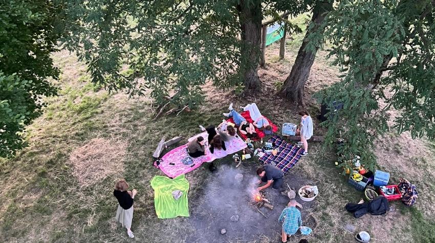 Menschen sind aus der Vogelperspektive auf Picknickdecken im Wald zu sehen. Es wird ein Lagerfeuer gemacht.