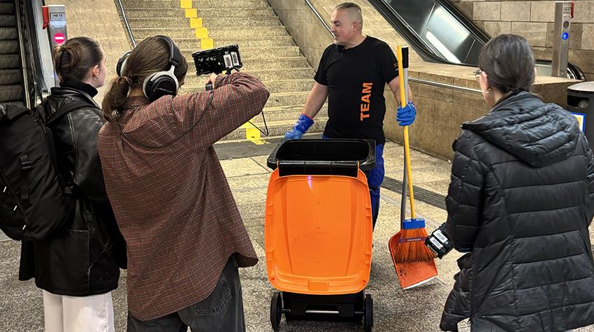 Studierendengruppe drehen ein Videointerview von einem Alltagshelden in einem U-Bahn Tunnel vor einer Rolltreppe