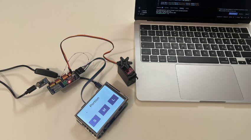 Zu sehen ist der Miniatur Computer "Raspberry Pi" und im Hintergrund ein Laptop mit einem geöffneten Programmierprogramm