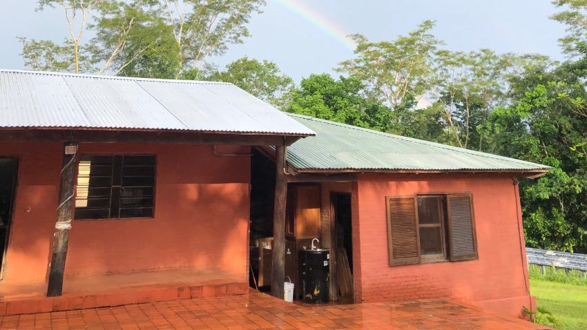 Man sieht eine paraguayische Küche, die "cocinita" von außen. Über ihr erscheint ein Regenbogen am Himmel. 