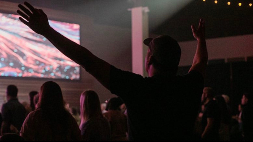 Ein Mann hebt seine Hände in die Höhe während er Kirchenlieder singt. 