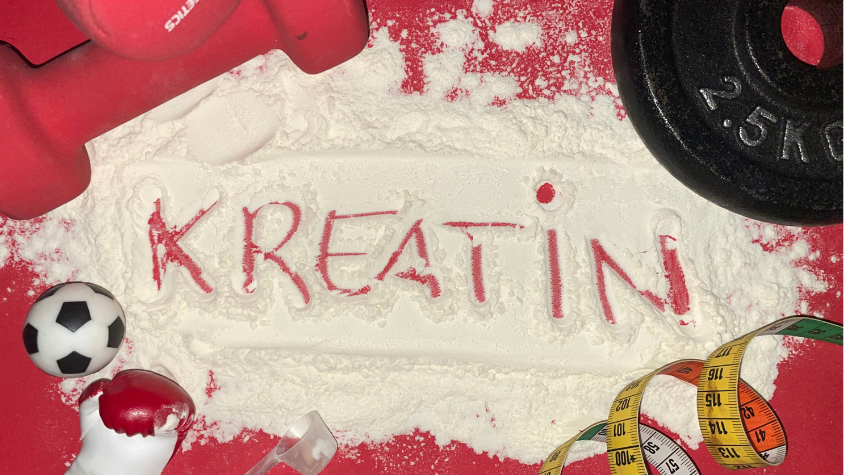 Das Wort "KREATIN" ist in weißem Pulver auf rotem Untergrund geschrieben, umgeben von einer roten Hantel, einer schwarzen Gewichtsscheibe, einem Maßband, einem kleinen Fußball und einem kleinen, roten Boxhandschuh.
