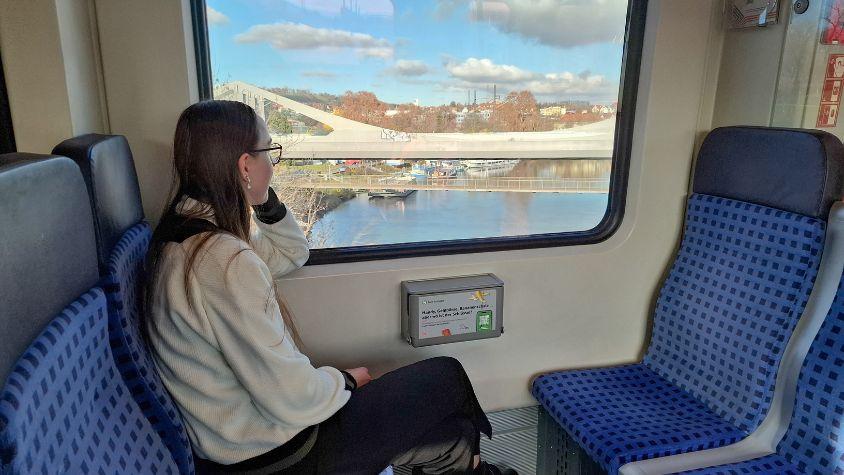 Junge Frau sitzt rechts im Bild in der Bahn und schaut aus dem Fenster.