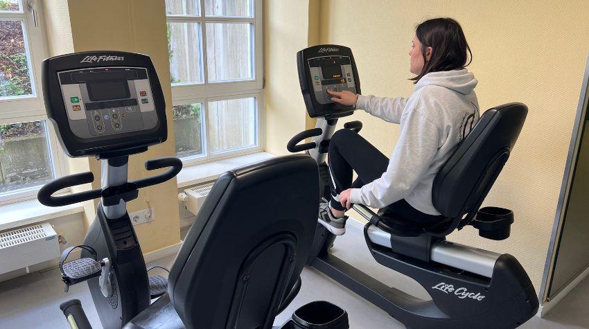 Eine Frau sitz auf dem Ergometer.