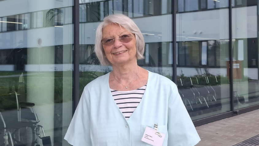 Die Grüne Dame lächelnd vor dem Krankenhaus.