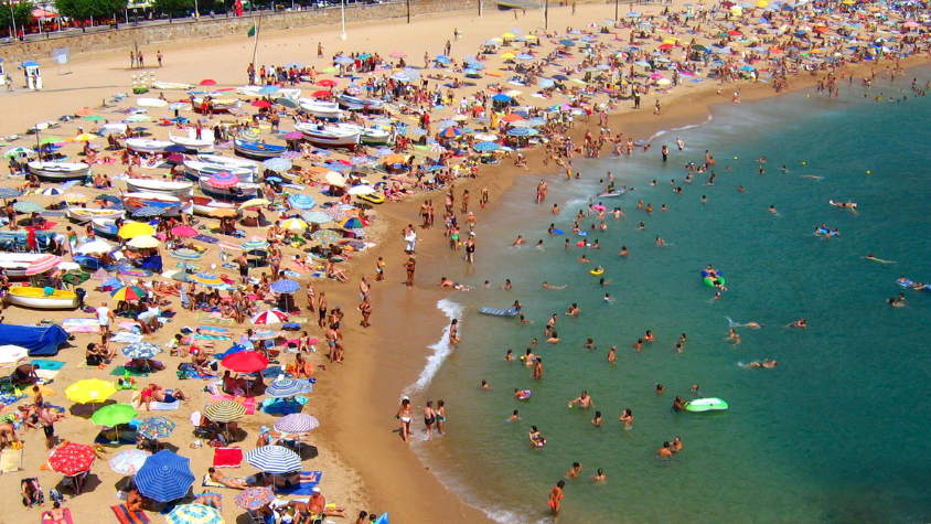 Crowded beach in Spain during peak summer season showing high tourist density along the coastline.