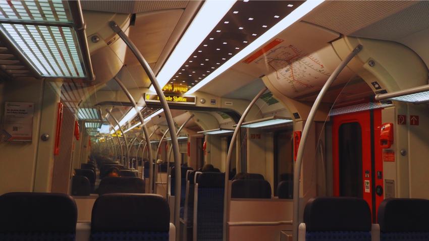 Auf dem Bild ist eine S-Bahn von innen zu sehen. Man sieht eher die Decke der S-Bahn und Sitzplätze, die zum Teil mit Menschen belegt sind.