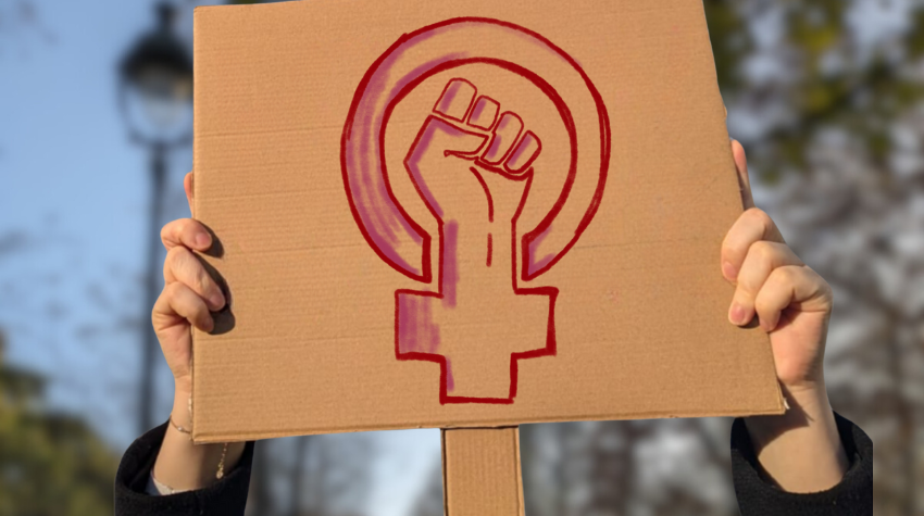 Zwei Hände halten ein Protest-Schild, in roter Farbe das Feminismus-Zeichen dargestellt ist.