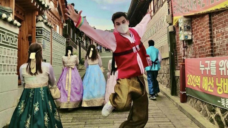 Henrik springt im koreanischen Hanbok in die Höhe, während Frauen hinter ihm ebenfalls traditionell koreanisch gekleidet sind.