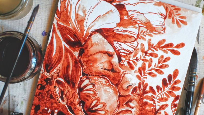Zu sehen ist ein Bild einer Frau gemalt mit Menstruationsblut. Daneben ein Glas mit Blut, worauf ein Pinsel abgelegt ist.