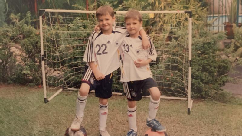 Henrik und sein Zwillingsbruder stehen in Fußballtrikots vor einem Tor in ihrem tropischen Garten.