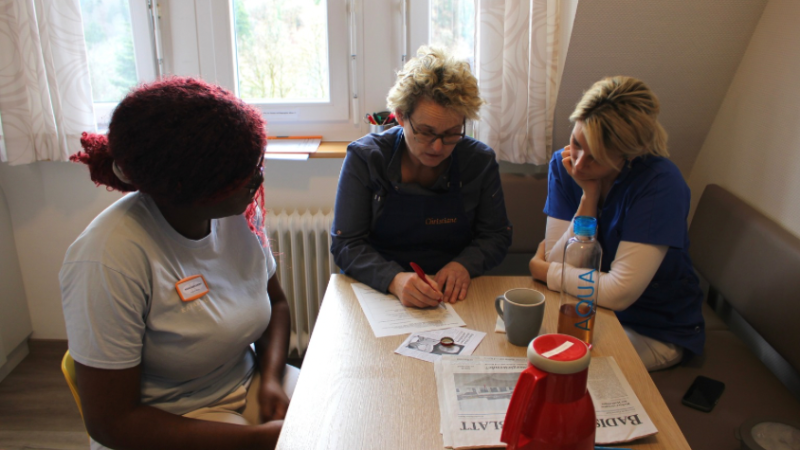Christiane Stangier sitzt mit den Pflegerinnen und bespricht das Essen für die Gäst*innen.
