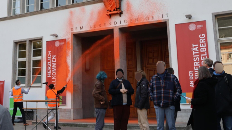 Orange Farbe wird bei einer Aktion der „Letzten Generation“ auf die Universität in Heidelberg gesprüht.