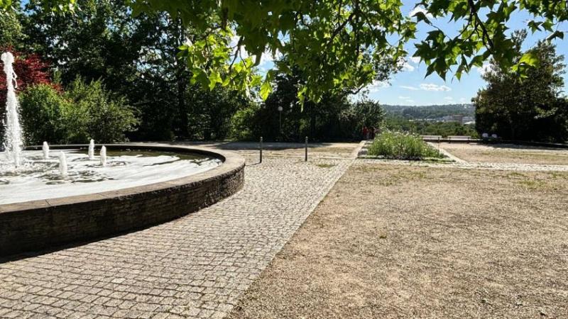 Zu sehen ist ein Brunnen im Oberen Kurpark. Im Hintergrund eine schöne Aussicht, jedoch gibt es nur seitlich ganz wenig Schatten.