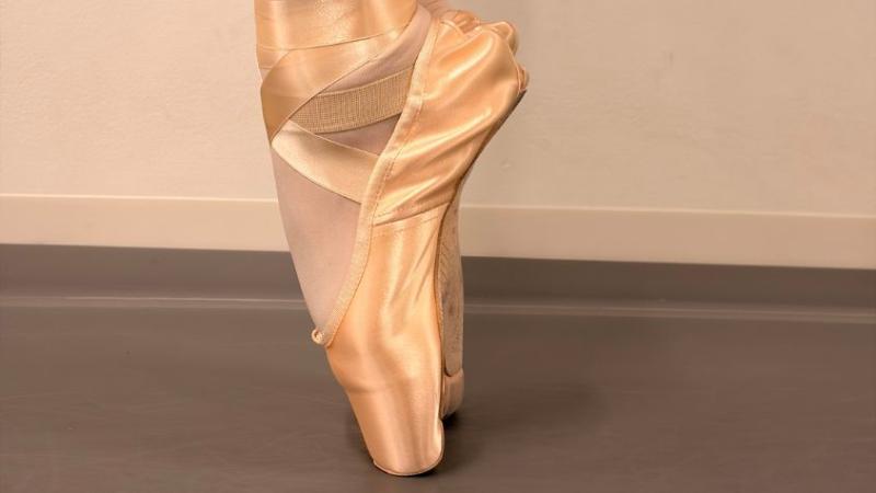 Eine Balletttänzerin steht seitlich gesehen auf Spitze in der sechsten Position mit parallel nebeneinanderstehenden Füßen und nach vorne gerichteten Fußspitzen.