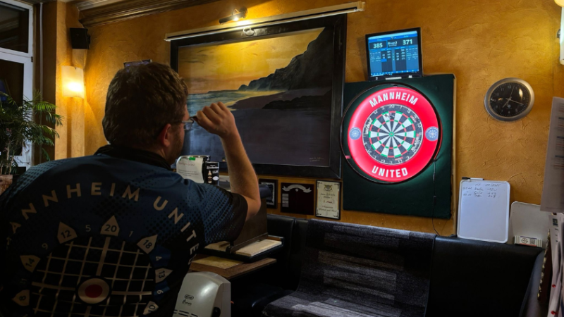 Ein Mann wirft auf eine beleuchtete Dartsscheibe