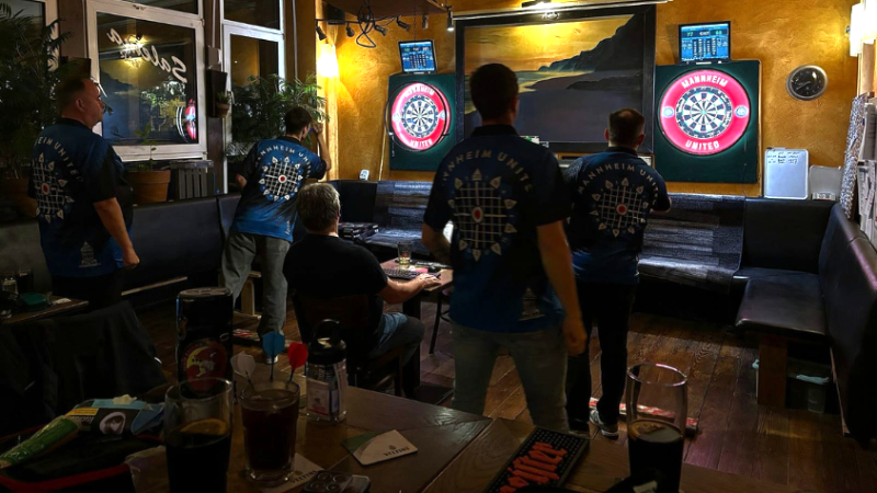 Etwas schrägerer Blick auf Darts spielende Männer an zwei Dartsscheiben 
