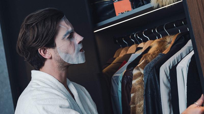 Ein Mann mit einer Tuchmaske schaut in seinen Kleiderschrank.
