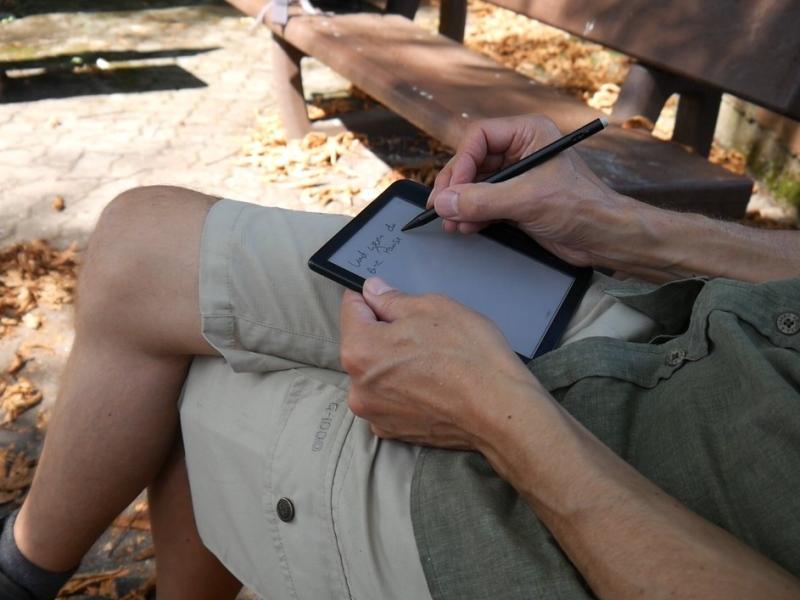 Ein Mann sitzt auf einer Bank und schreibt in ein E-Book.