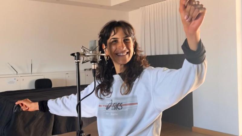 Jasmin steht alleine vor dem Mikrofon und singt. Währenddessen hat sie einen Arm ausgestreckt und den anderen oben.
