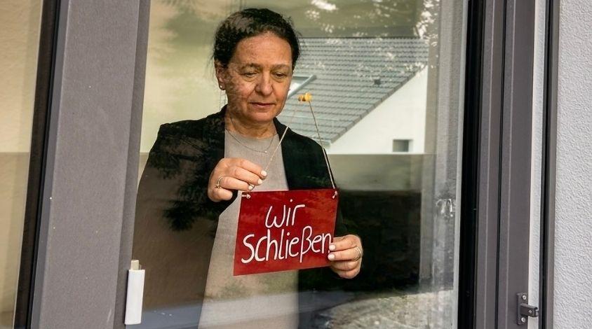 Frau hängt Wir schließen-Schild an Ladentür